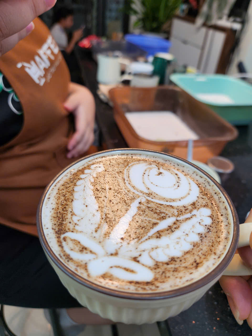 Ly cappuccino tạo hình hoa hồng bằng latte art kết hợp rắc bột cacao, thể hiện sự tinh tế và sáng tạo trong kỹ thuật trình bày